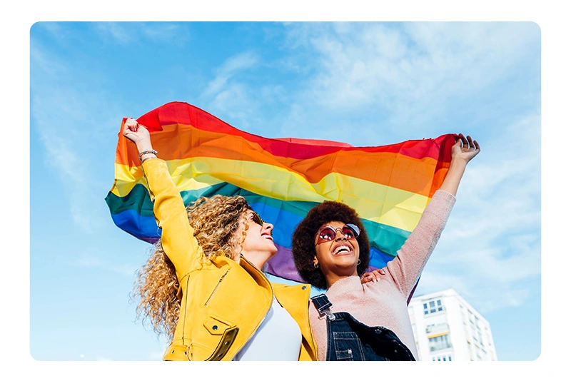 two women hodling a rainbow flag together to celebrate pride month
